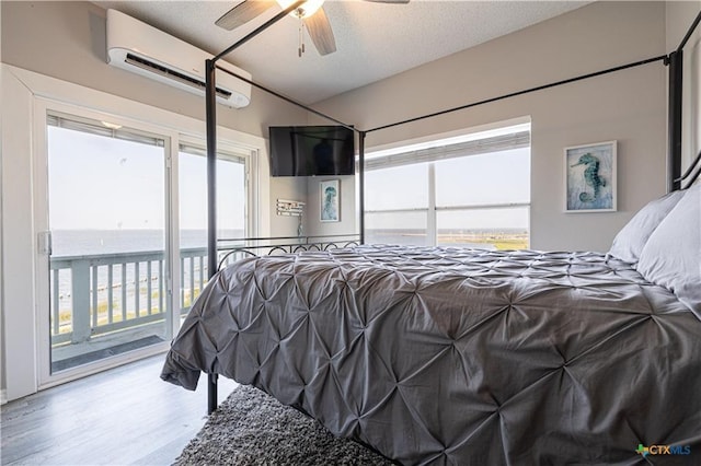 106 Clement Cv, Port Lavaca, TX 77979 - bedroom featuring a textured ceiling, a wall unit AC, ceiling fan, access to exterior, and wood finished floors