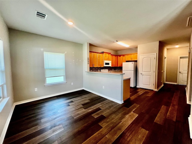 kitchen with white appliances, dark wood-type flooring, visible vents, a peninsula, and baseboards