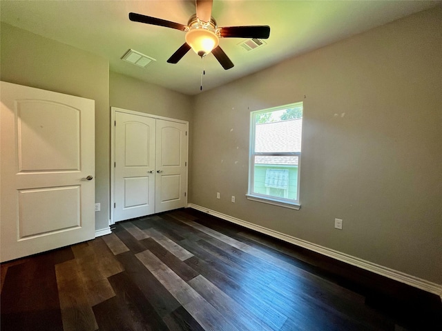 unfurnished bedroom featuring a closet, visible vents, baseboards, and dark wood finished floors