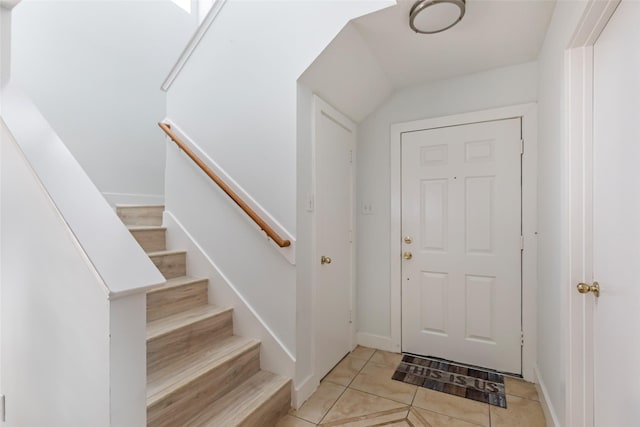 foyer entrance featuring baseboards, stairs, and light tile patterned floors