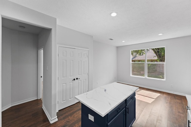 kitchen with light stone countertops, dark wood-type flooring, a kitchen island, baseboards, and blue cabinets