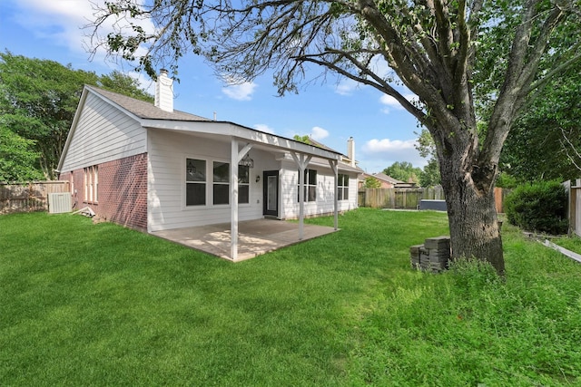 back of house featuring a patio area, a yard, a chimney, brick siding, and fence