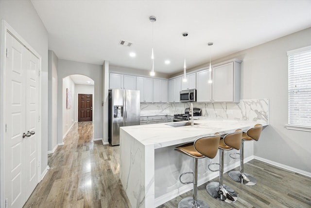 kitchen with arched walkways, light wood-style flooring, stainless steel appliances, visible vents, and a peninsula