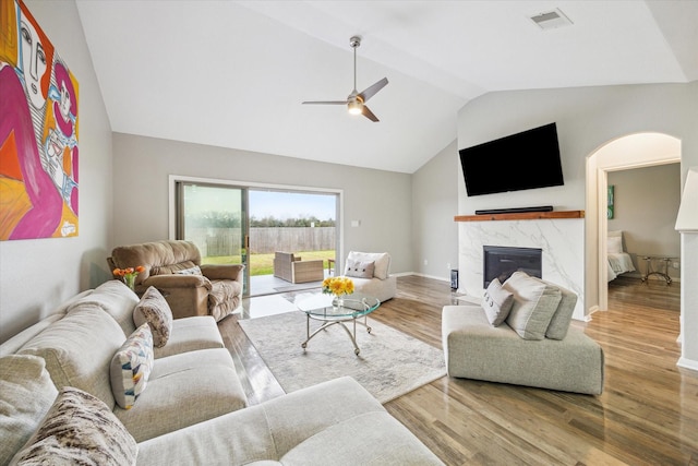 living area with ceiling fan, visible vents, vaulted ceiling, a high end fireplace, and wood finished floors