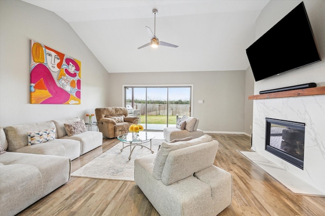 living area with ceiling fan, high vaulted ceiling, a high end fireplace, and light wood-style floors
