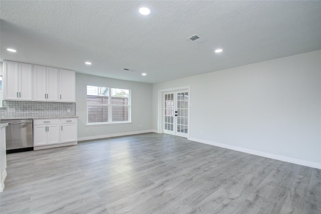 unfurnished living room with baseboards, visible vents, a textured ceiling, and light wood finished floors