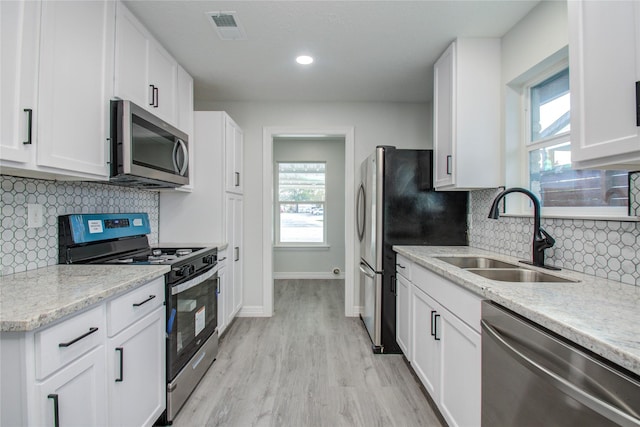 kitchen featuring appliances with stainless steel finishes, light wood finished floors, a sink, white cabinetry, and visible vents