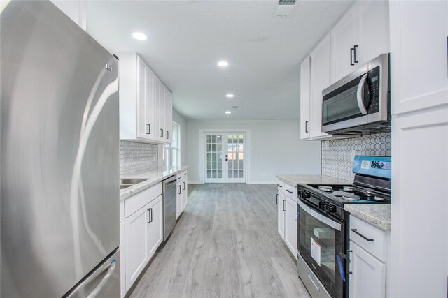 kitchen featuring stainless steel appliances, decorative backsplash, visible vents, light wood-style flooring, and baseboards