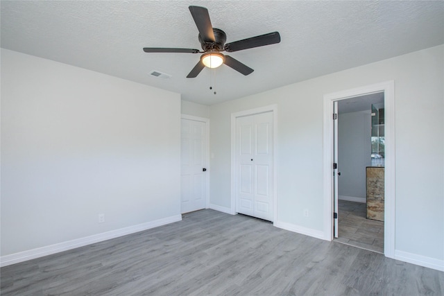 unfurnished bedroom featuring a textured ceiling, visible vents, a closet, baseboards, and wood finished floors