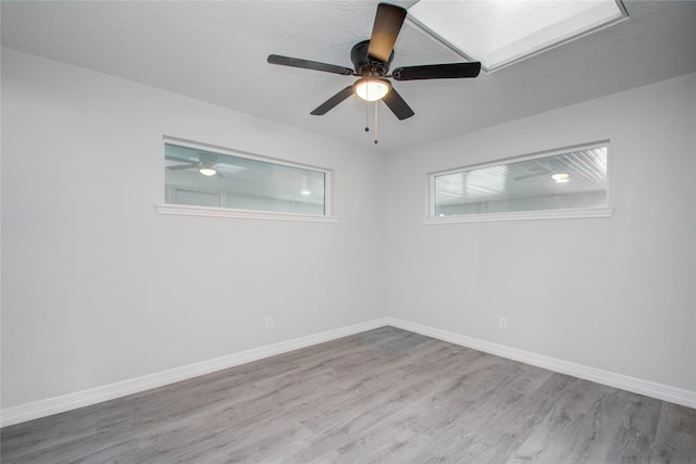 unfurnished room with baseboards, wood finished floors, a ceiling fan, and a skylight