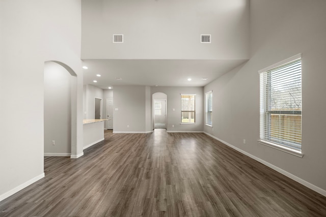 9993 Mountain Lion Ln, Magnolia, TX 77354 - unfurnished living room with visible vents, dark wood-style floors, baseboards, arched walkways, and a towering ceiling