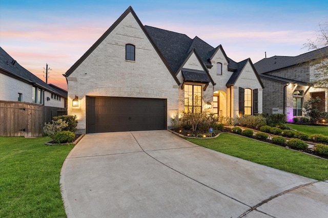 french provincial home featuring an attached garage, concrete driveway, a front yard, and brick siding