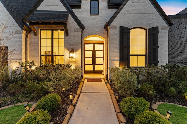 exterior entry at dusk with brick siding and roof with shingles