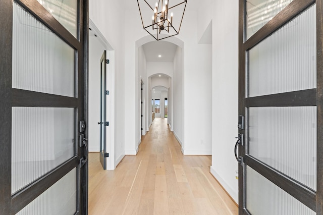 hallway featuring baseboards, light wood-type flooring, arched walkways, and a towering ceiling