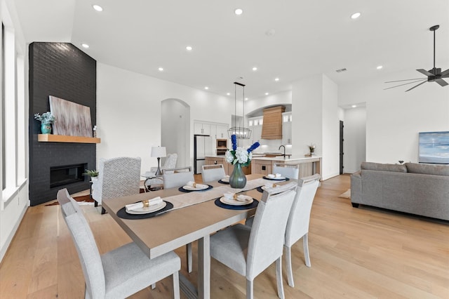 dining area with recessed lighting, a large fireplace, light wood-style floors, ceiling fan, and arched walkways