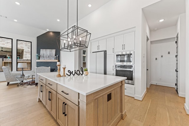 kitchen with appliances with stainless steel finishes, a kitchen island, light wood-style flooring, and a notable chandelier