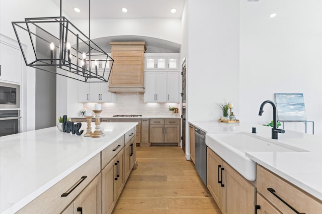 kitchen featuring a sink, stainless steel appliances, decorative backsplash, light wood-style flooring, and pendant lighting