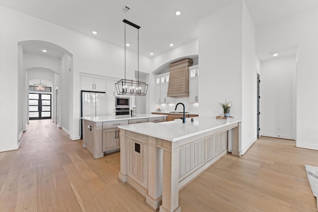 kitchen featuring light wood-style floors, stainless steel appliances, light countertops, arched walkways, and an island with sink