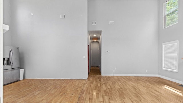 unfurnished living room with a towering ceiling, visible vents, baseboards, and light wood-style floors
