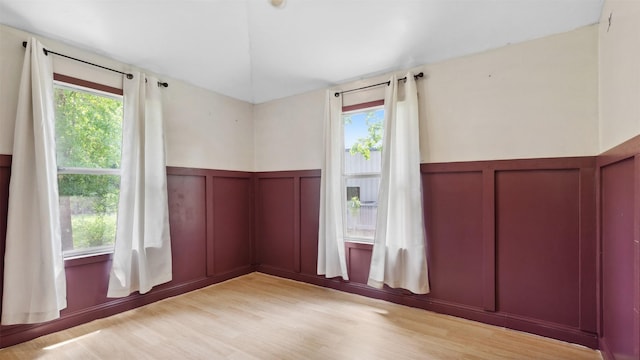empty room with a wealth of natural light, a decorative wall, light wood-style flooring, and wainscoting