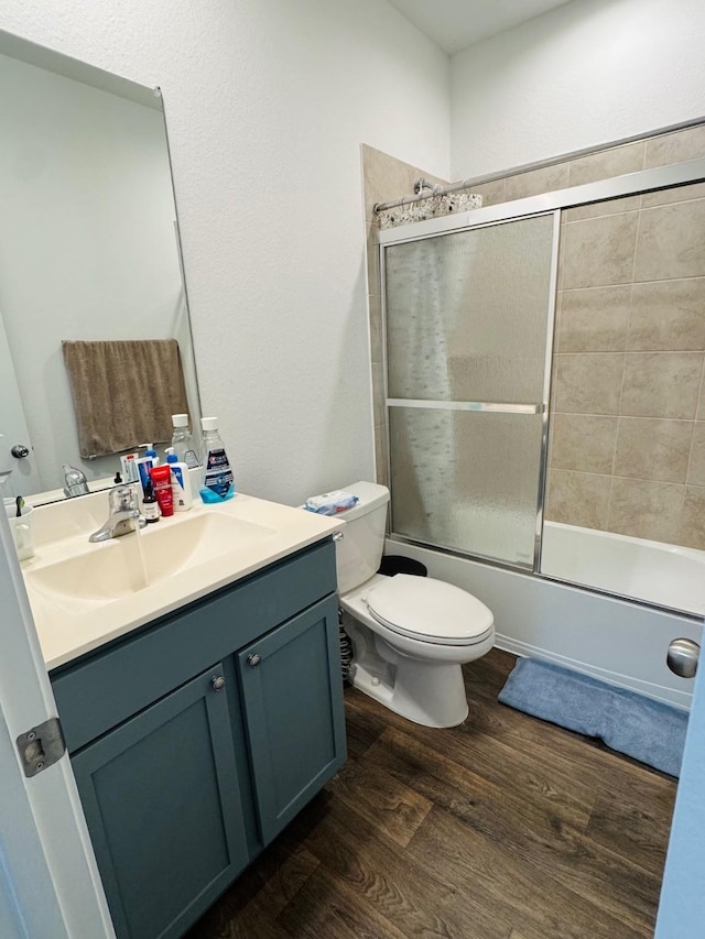 full bathroom with toilet, wood finished floors, bath / shower combo with glass door, and vanity