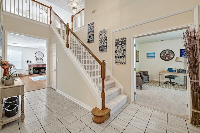 5127 Plantation Colony Dr, Sugar Land, TX 77478 - stairs featuring tile patterned flooring, carpet floors, a brick fireplace, baseboards, and a towering ceiling