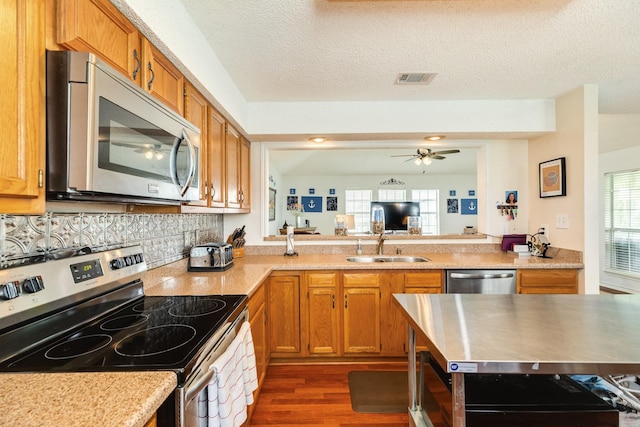 kitchen with appliances with stainless steel finishes, visible vents, brown cabinetry, and a sink