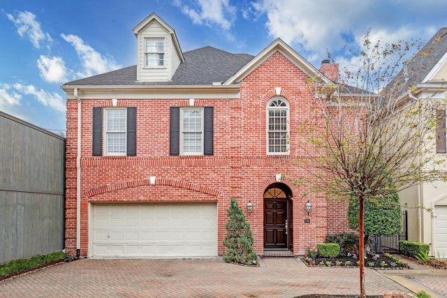 view of front of home with decorative driveway, a chimney, brick siding, a shingled roof, and an attached garage