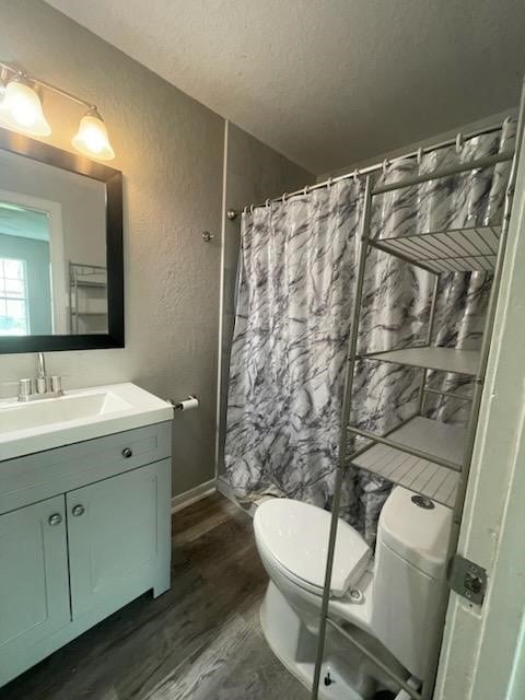 full bathroom featuring a textured wall, a shower with shower curtain, toilet, wood finished floors, and vanity
