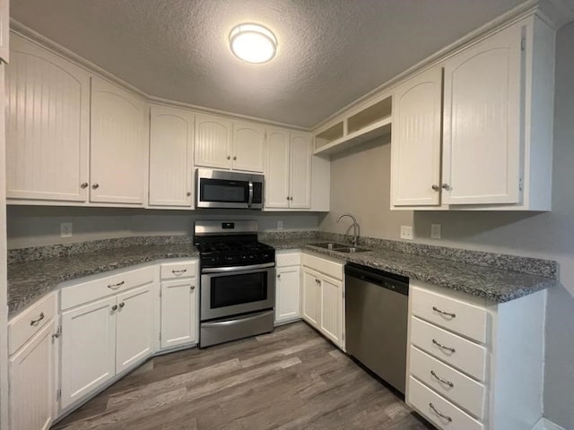 kitchen featuring stainless steel appliances, white cabinets, a sink, dark wood-style floors, and a textured ceiling