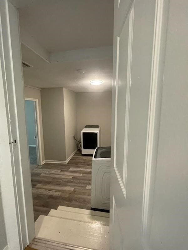 corridor featuring wood finished floors, washer / dryer, and baseboards