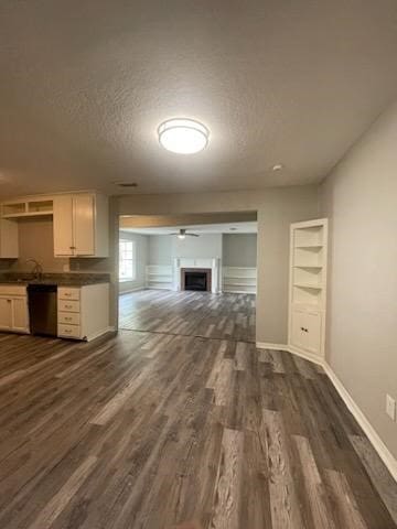 unfurnished living room with a textured ceiling, baseboards, a fireplace, dark wood-type flooring, and a ceiling fan