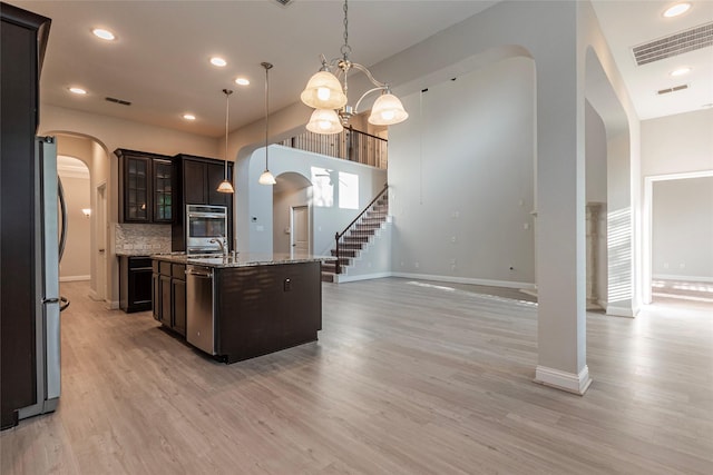3302 Indigo Acres Ct, Katy, TX 77494 - kitchen with stainless steel appliances, dark brown cabinetry, visible vents, arched walkways, and an island with sink