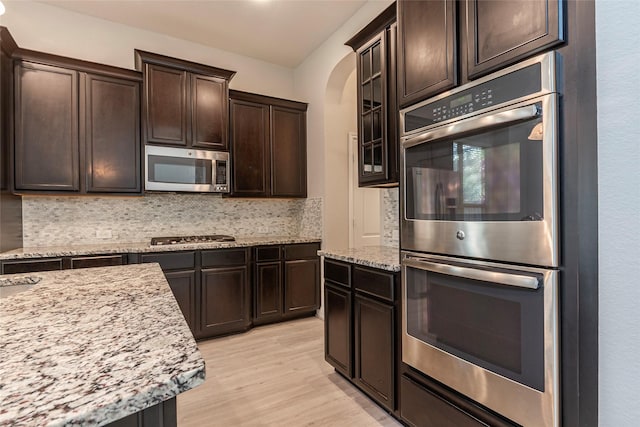 3302 Indigo Acres Ct, Katy, TX 77494 - kitchen with dark brown cabinetry, tasteful backsplash, light stone counters, appliances with stainless steel finishes, and light wood-type flooring