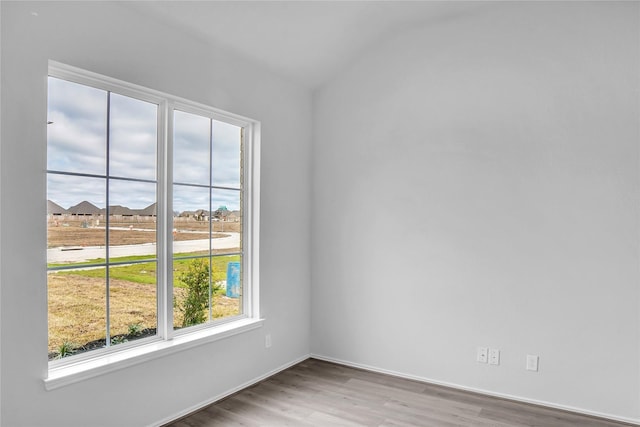empty room featuring vaulted ceiling, wood finished floors, and baseboards