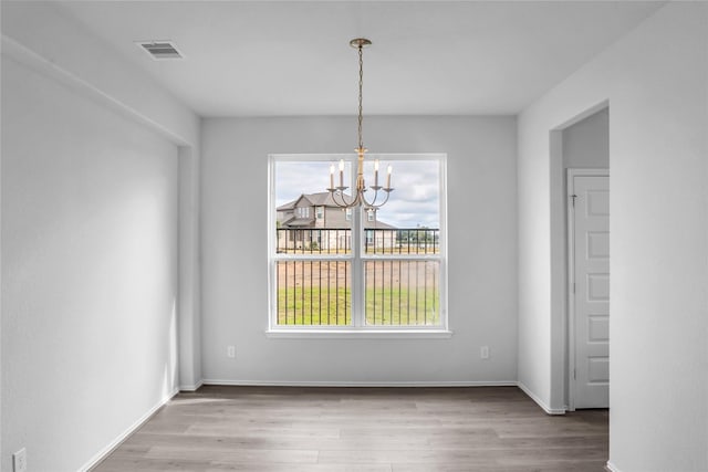unfurnished dining area with an inviting chandelier, wood finished floors, visible vents, and baseboards