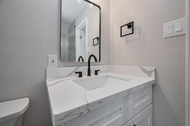 half bath featuring toilet, a textured wall, and vanity