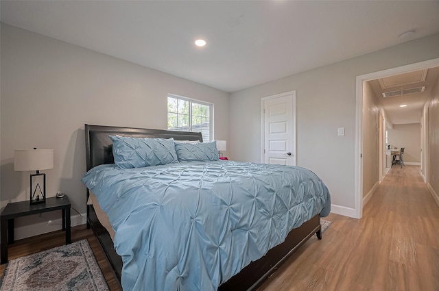 bedroom featuring baseboards, light wood-type flooring, attic access, and visible vents