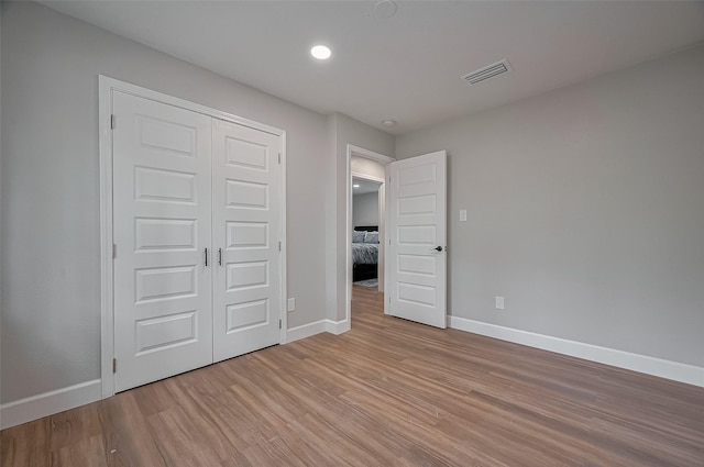 unfurnished bedroom with baseboards, visible vents, light wood-style floors, and a closet