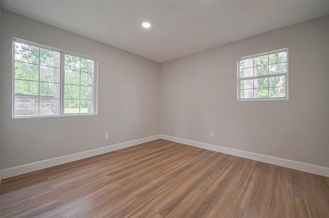 empty room featuring baseboards, recessed lighting, a wealth of natural light, and light wood finished floors