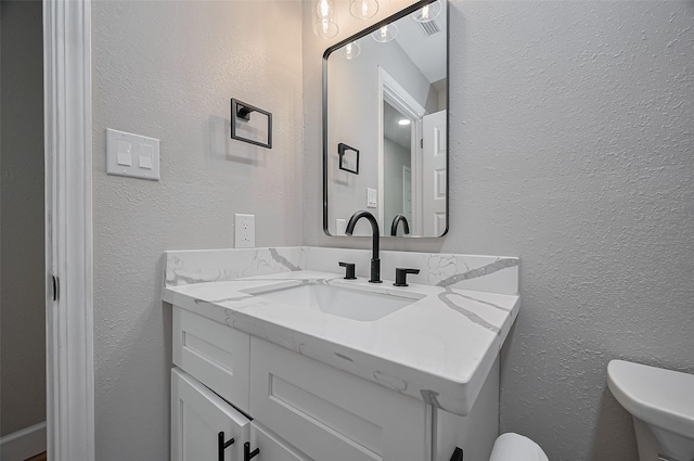 bathroom with a textured wall, toilet, visible vents, and vanity