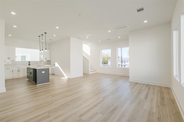 unfurnished living room with visible vents, baseboards, stairway, light wood-type flooring, and recessed lighting