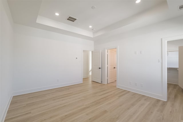 unfurnished bedroom with a walk in closet, visible vents, a raised ceiling, baseboards, and light wood finished floors