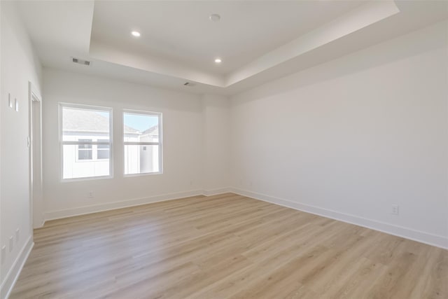 empty room featuring recessed lighting, a tray ceiling, light wood-type flooring, and visible vents