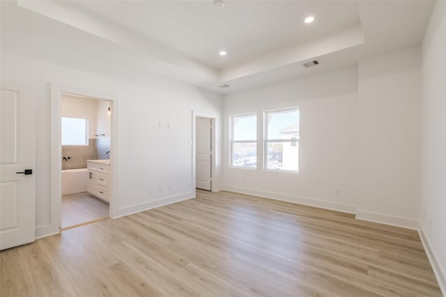 unfurnished bedroom with visible vents, baseboards, recessed lighting, a tray ceiling, and light wood-style flooring
