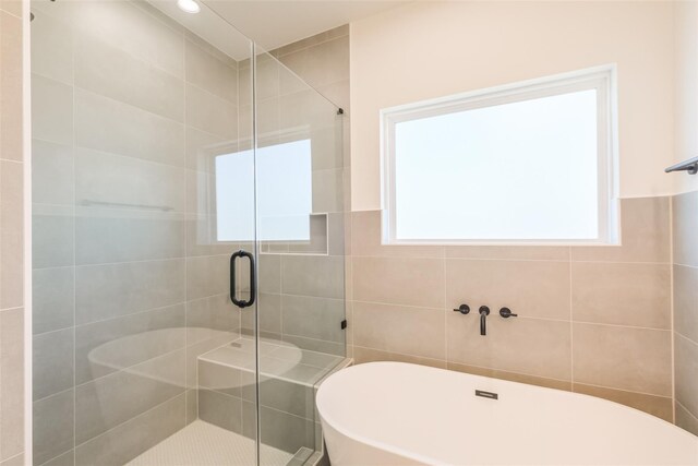 bathroom featuring a healthy amount of sunlight, a freestanding tub, a stall shower, and tile walls