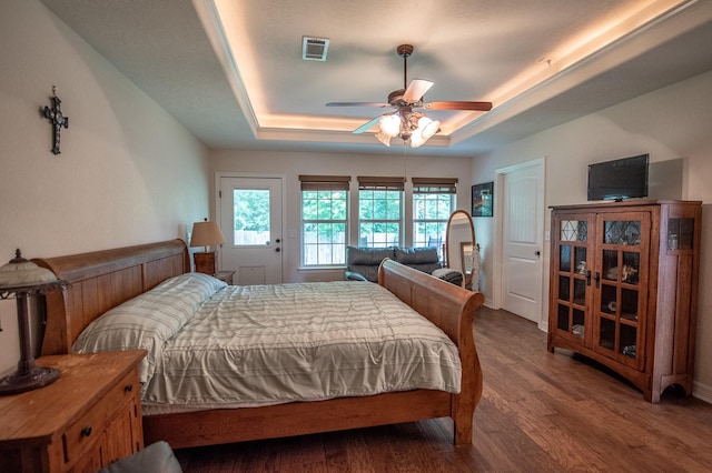 bedroom with visible vents, ceiling fan, wood finished floors, and a tray ceiling