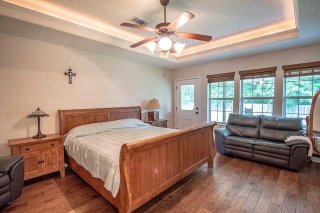 bedroom featuring a ceiling fan, a tray ceiling, wood finished floors, and visible vents