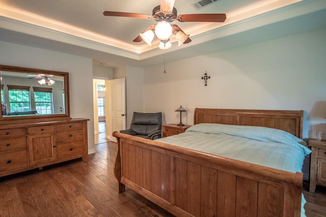 bedroom with a raised ceiling, a ceiling fan, wood finished floors, and visible vents