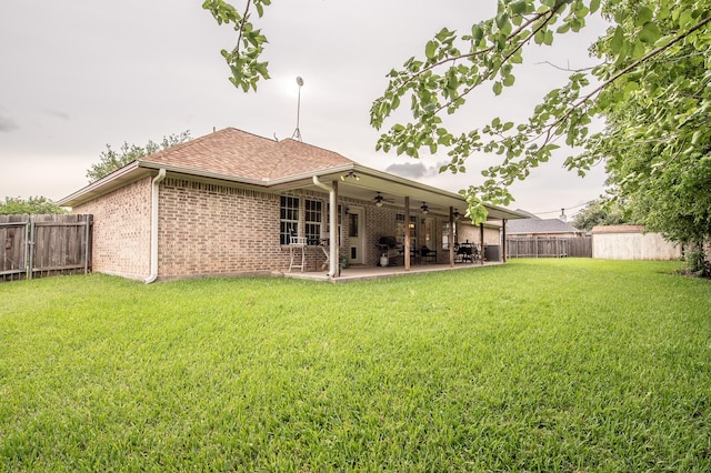 rear view of property with a fenced backyard, a ceiling fan, a lawn, and brick siding